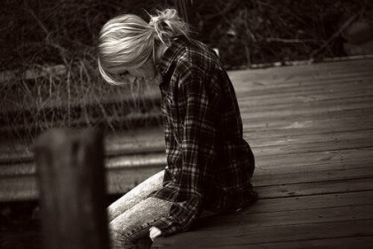 Ein junges Mädchen sitzt nachdenklich auf einem Steg.