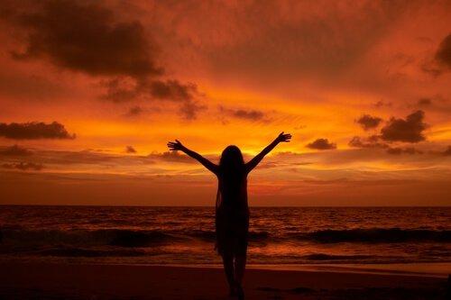 Frau am Meer streckt ihre Arme gen Himmel