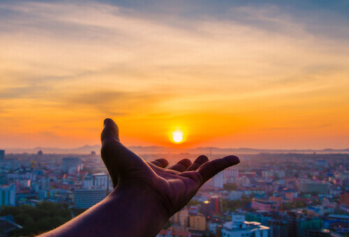 Hand hält untergehende Sonne über einer Stadt