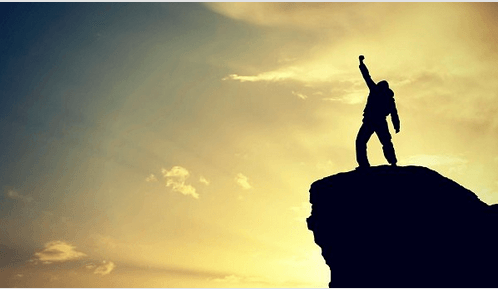 Erfolg: Person auf einem Felsen streckt ihren Arm gen Himmel.