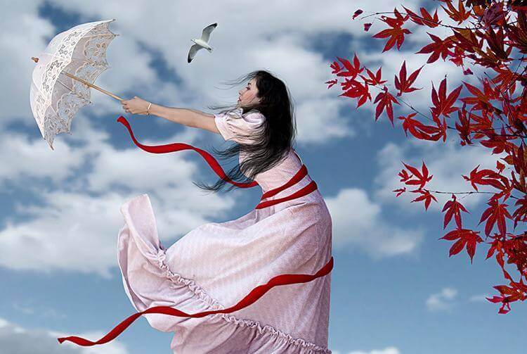 Eine Frau mit einem Schirm vor einem roten Ahorn