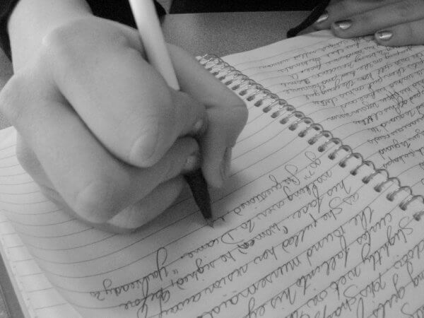 Eine Frau verfasst einen handschriftllichen Eintrag in ein liniertes Ringbuch.
