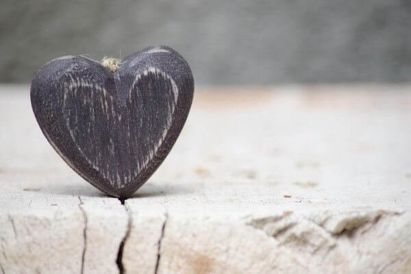 Das Gesetz der Anziehung - Kleines Herz aus Holz steckt in einem Holzspalt.