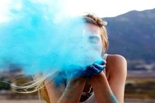 Frau mit einem gesunden Selbstwertgefühl bläst blauen Staub in die Kamera