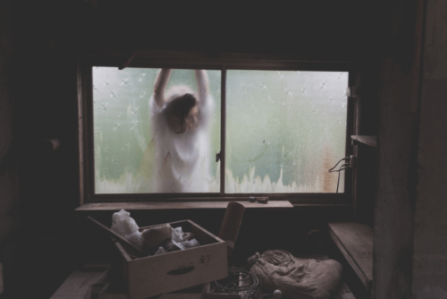 Frau steht am Fenster eines lange nicht aufgeräumten Zimmers