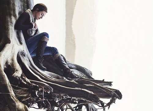 Frau in Winterkleidung auf einer Baumwurzel