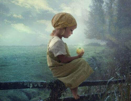 Mädchen auf einem Zaun hält einen gelben Apfel in der Hand