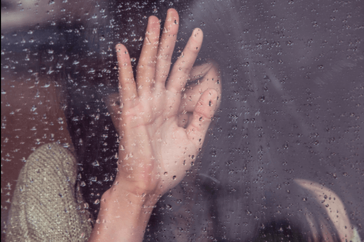 Ängstliche Frau lehnt an Fensterscheibe