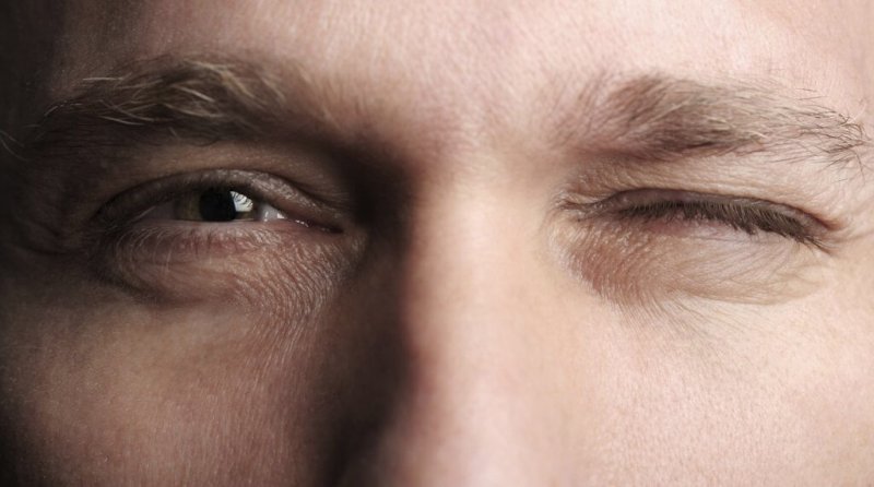 Mann kneift ein Auge zu