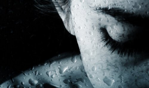Frau mit geschlossenen Augen hinter nasser Scheibe