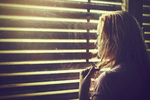 Frau blickt durch Jalousien ins Licht.