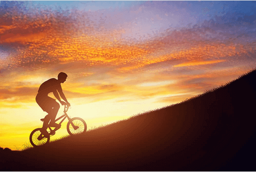 Mann fährt im Sonnenuntergang auf dem Fahrrad einen Berg hinauf.