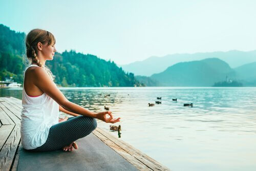Eine junge Frau meditiert an einem See. 