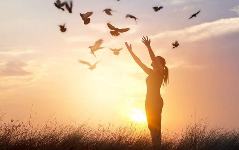 Frau streckt ihre Hände zu fliegenden Tauben aus