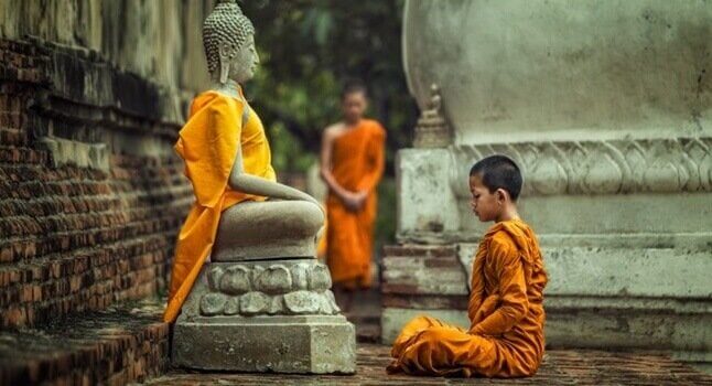 Junger Mönch sitzt vor einer Buddhastatue