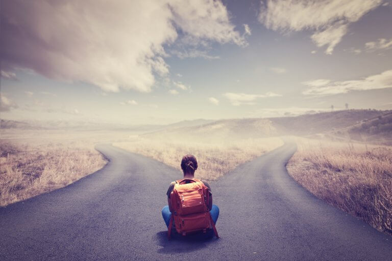 Frau, die mit großem Rucksack an einer Weggabelung sitzt