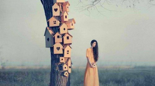 Nachdenkliche Frau, die neben einem Baum voller Vogelhäuser steht