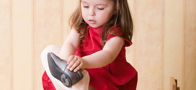 Ein kleines Mädchen zieht seinen rechten Schuh an.