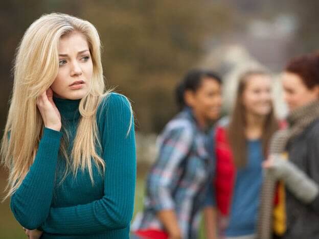 Eine Frau steht abseits von anderen Menschen. Sie fühlt sich unwohl.