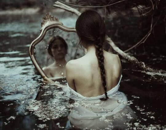 Frau betrachtet sich im Spiegel, das Wasser steht ihr bis zur Brust