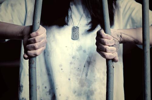 Eine Gefängnisinsassin biegt die Stäbe des Gitters auf.