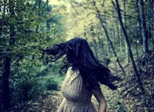 Eine Frau rennt durch einen Wald und dreht sich panisch um. 