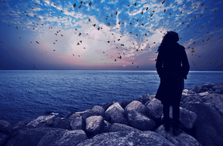 Eine Frau schaut auf den friedlichen Ozean. Der Himmel ist mit wenigen Wolken bedeckt.
