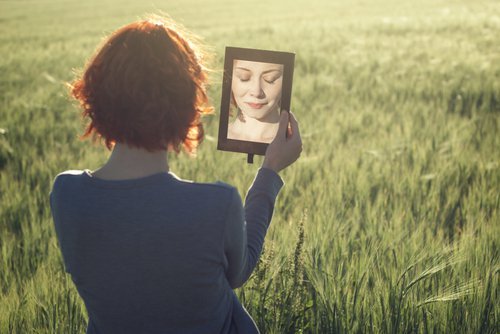 Frau steht im Getreidefeld und betrachtet sich im Spiegel