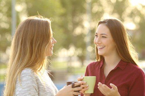 Zwei Freundinnen führen ein erheiterndes Gespräch mit Kaffeetassen in der Hand.