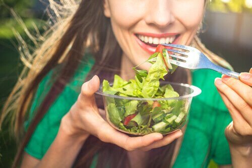 Eine gesunde Frau mit einem grünen T-Shirt isst einen leckeren Salat, um ihr Immunsystem zu stärken.