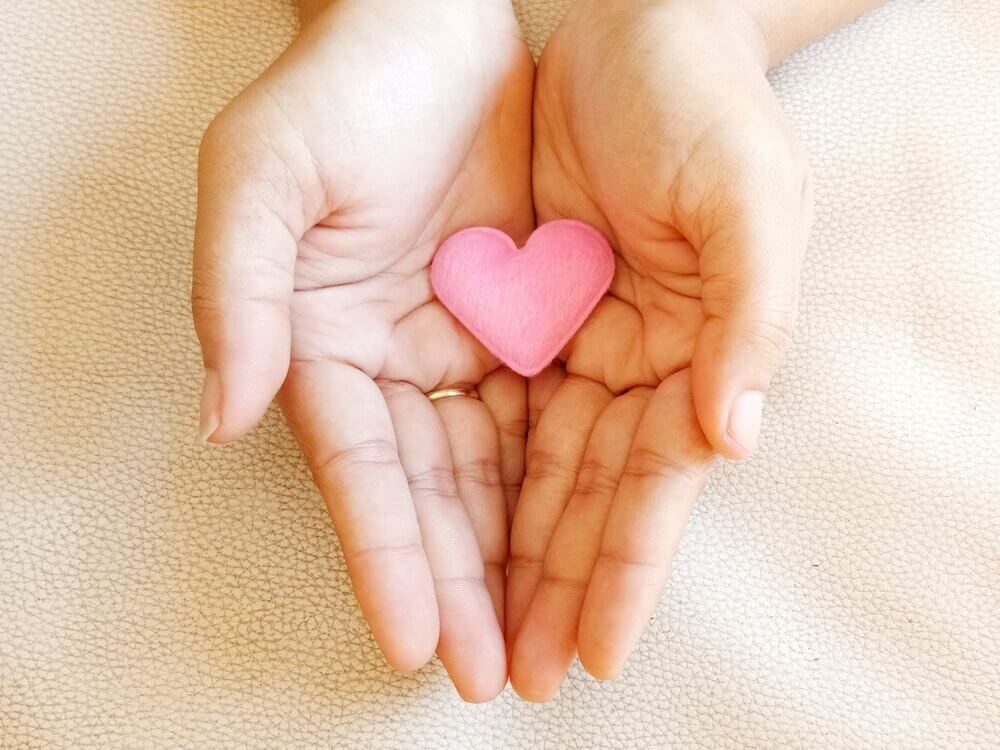 Zwei Hände halten ein rosa Herz aus Stoff.