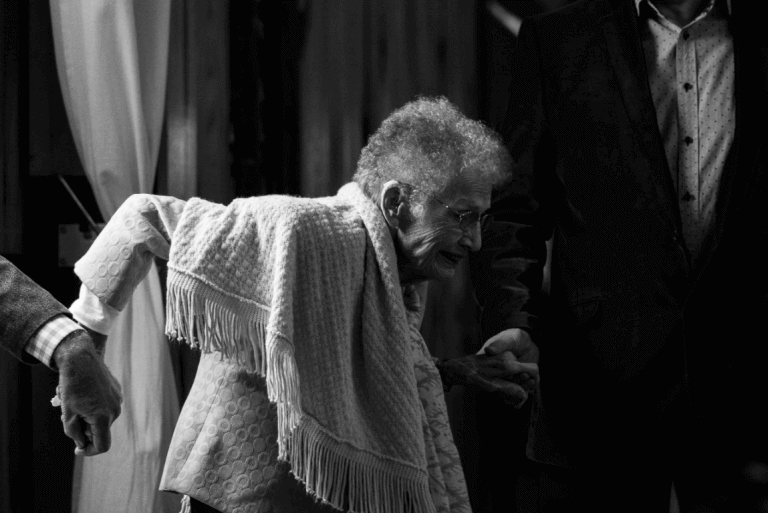 Alte Frau geht an den Händen zweier Helfer