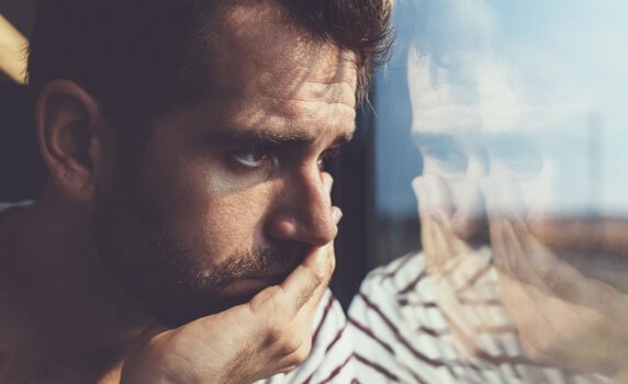 Mann blickt traurig durch ein Fenster