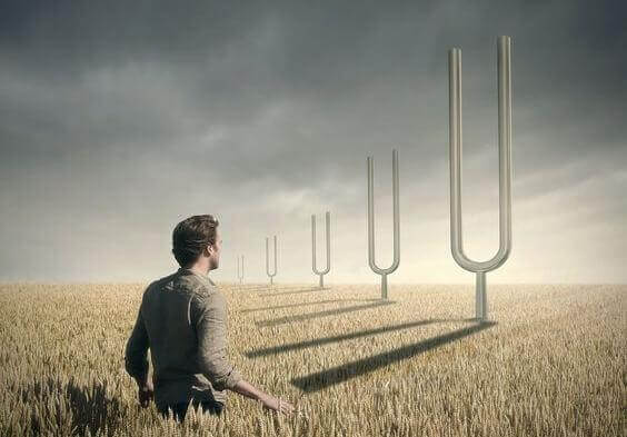 Mann steht in Getreidefeld und blickt auf fünf gigantisch große Stimmgabeln.