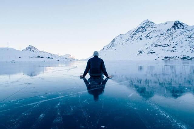 Mann sitzt auf zugefrorenem See vor Bergen