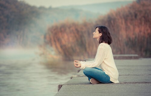 Eine Frau sitzt meditierend an einem friedlichen See.