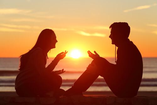 Ein Paar sitzt am Strand bei Sonnenuntergang und unterhält sich.