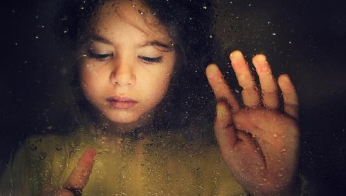 Ein trauriges Kind malt mit den Fingern auf einer verregneten Fensterscheibe.