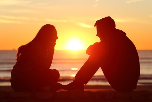 Zwei Freunde sitzen am Strand bei Sonnenuntergang und reden