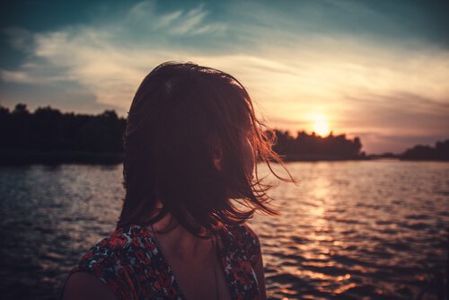 Eine Frau schaut hinaus auf einen See, während die Sonne untergeht
