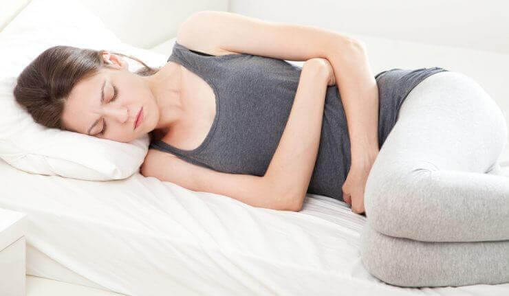 Frau liegt mit Bauchschmerzen auf dem Bett