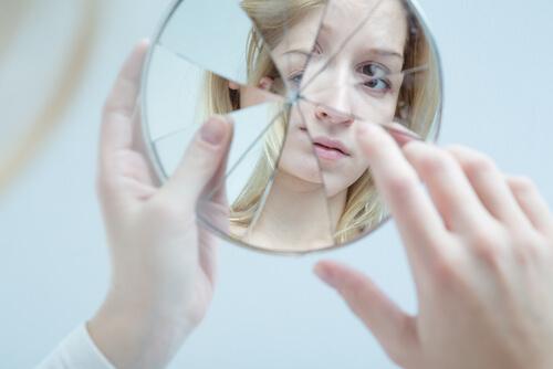 Eine junge, blonde Frau schaut in einen zerbrochenen Spiegel.
