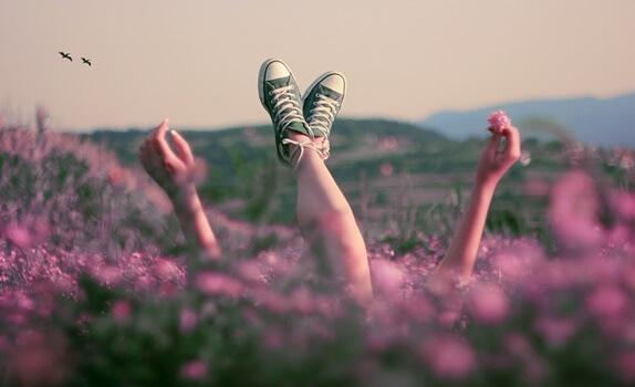 Frau streckt auf einer pinken Blumenwiese ihre Beine und Hände nach oben