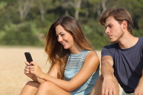 Mann schaut eifersüchtig zu seiner Freundin, die Nachrichten auf ihrem Telefon liest