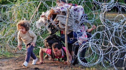 Flüchtlinge kriechen unter einem Zaun durch