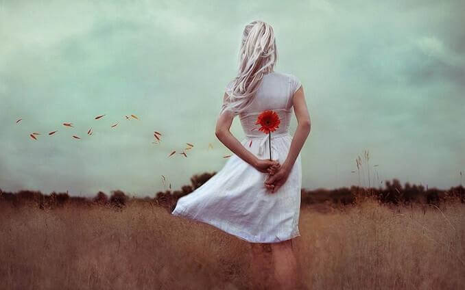 Blonde Frau hält hinter ihrem Rücken eine rote Blume