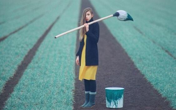 Frau steht mit einem großen Pinsel auf einem Rasen