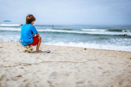 Junge sitzt auf einem Ball am Strand