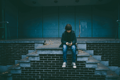 Trauriges Kind sitzt auf einer Treppe und schaut auf sein Telefon