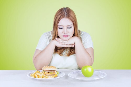 Eine Frau kann sich nicht entscheiden, ob sie lieber den Apfel oder den Burger essen soll